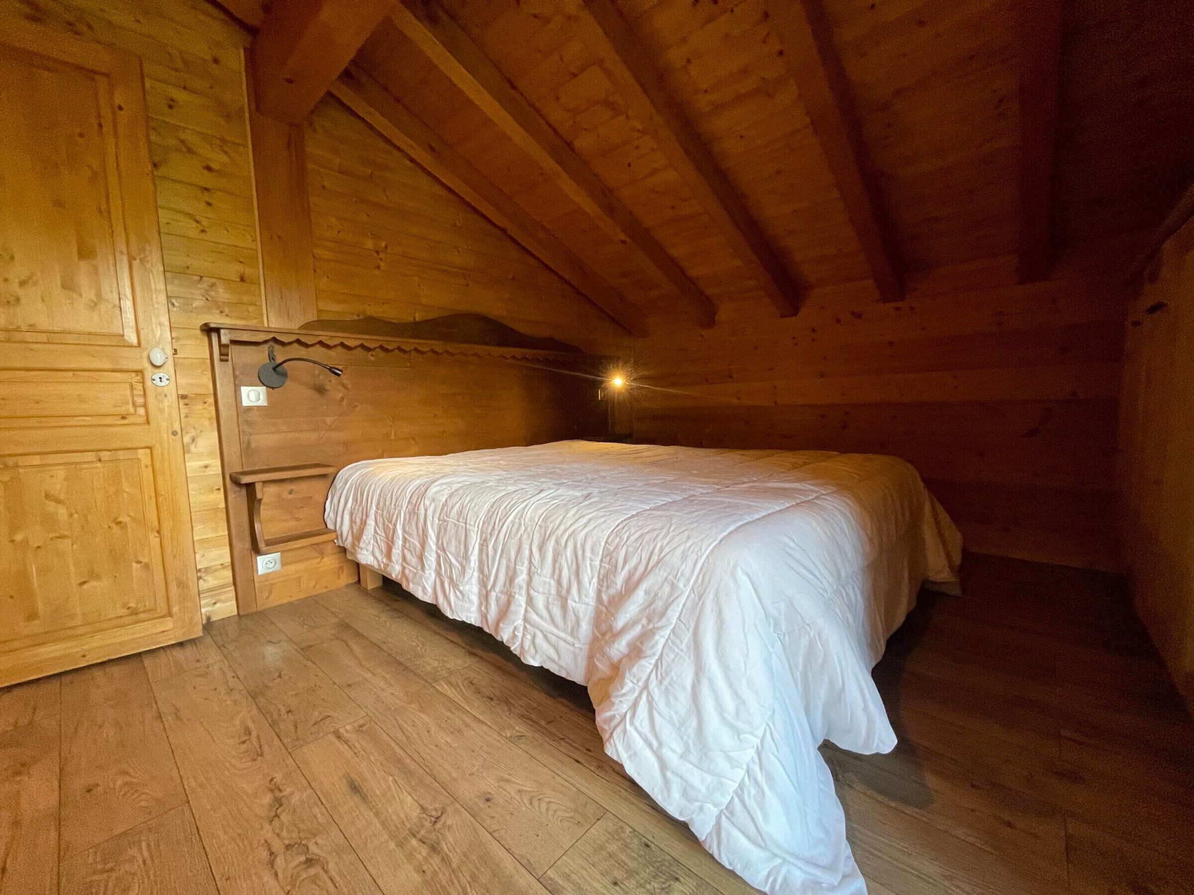 Une chambre dans une cabane en bois, avec un lit simple, des murs en bois et un plafond en pente.