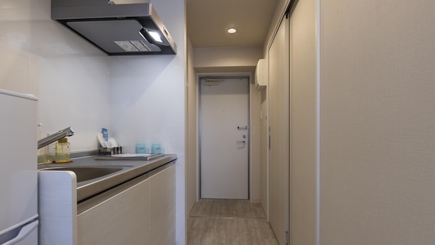 Un couloir étroit, avec un coin cuisine sur la gauche, comprenant un évier, un plan de travail et des placards. Une porte est visible au fond du couloir.