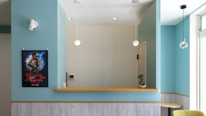 Un espace d’accueil avec un mur bleu clair, un comptoir d’accueil en bois, une affiche et un fauteuil vert.