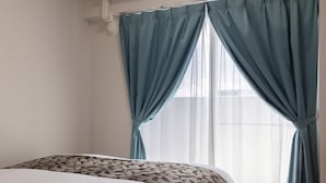 Une chambre d’hôtel avec un lit, une fenêtre avec des rideaux et un luminaire fixé au mur.