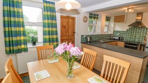A modern kitchen with a wooden island, a dining table with chairs, and a vase of flowers. - Garreg Lwyd Farm (Pwllheli)