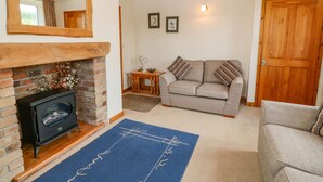 A living room with a fireplace, a sofa, a small table, and a door. - Garreg Lwyd Farm (Pwllheli)