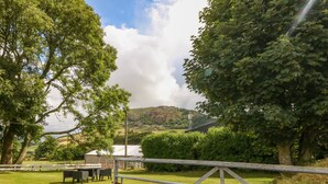 A rural landscape with a fenced area, a table and chairs, and a building in the background. - Garreg Lwyd Farm (Pwllheli)