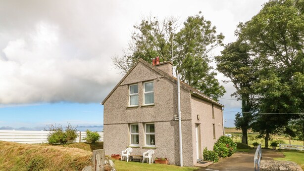 A two-story stone house with a paved driveway leading to a white door. - Garreg Lwyd Farm (Pwllheli)