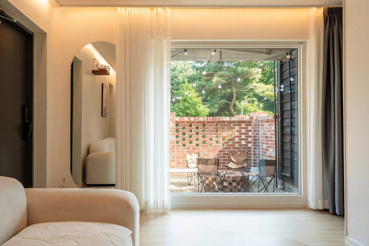A modern room with a sofa, a large mirror, and a view of a brick wall and outdoor seating.
