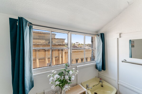 Un baño con ventana, lavamanos y espejo.