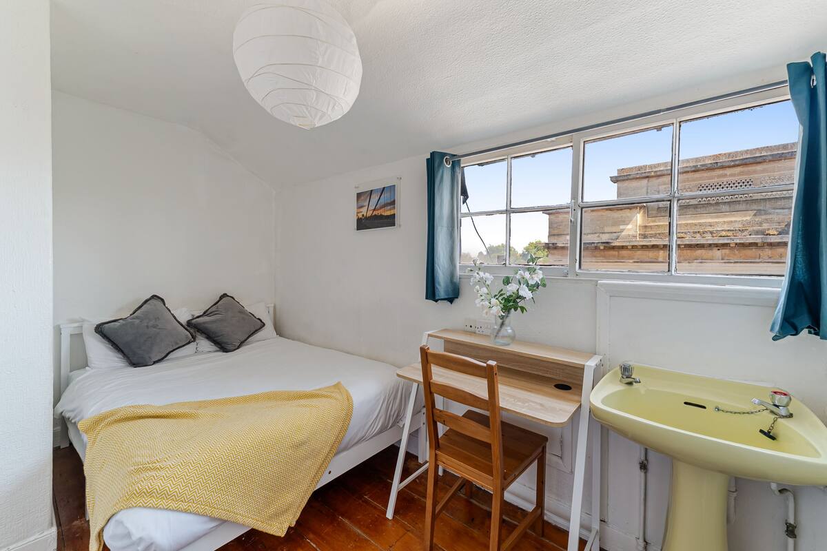 Un dormitorio con cama, escritorio, silla, ventana con cortinas y lavamanos.