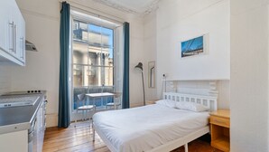 Una habitación pequeña con cama, escritorio y ventana que da a un edificio.