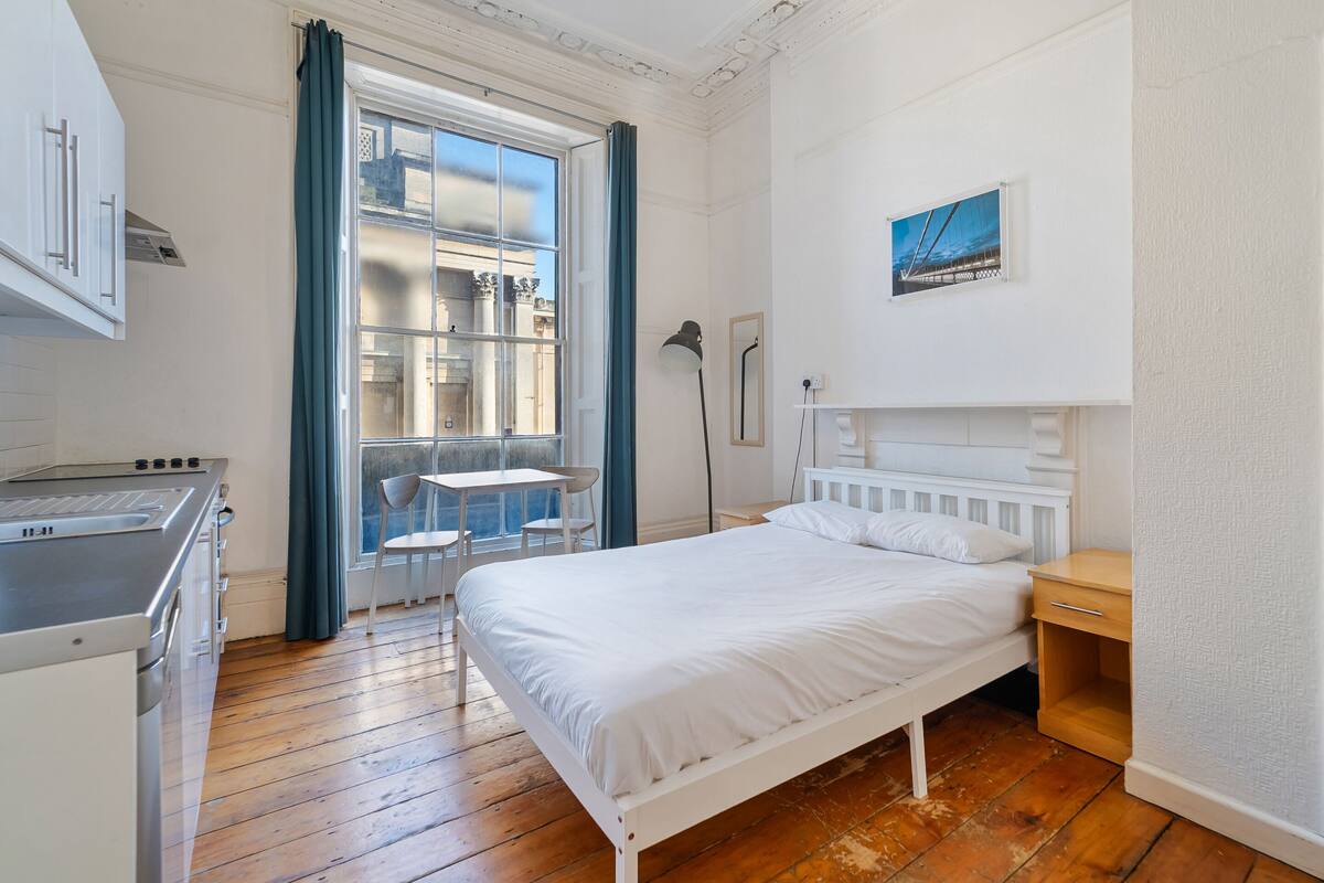 Una habitación pequeña con cama, escritorio y ventana que da a un edificio.