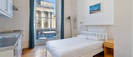Una habitación pequeña con cama, escritorio y ventana que da a un edificio.