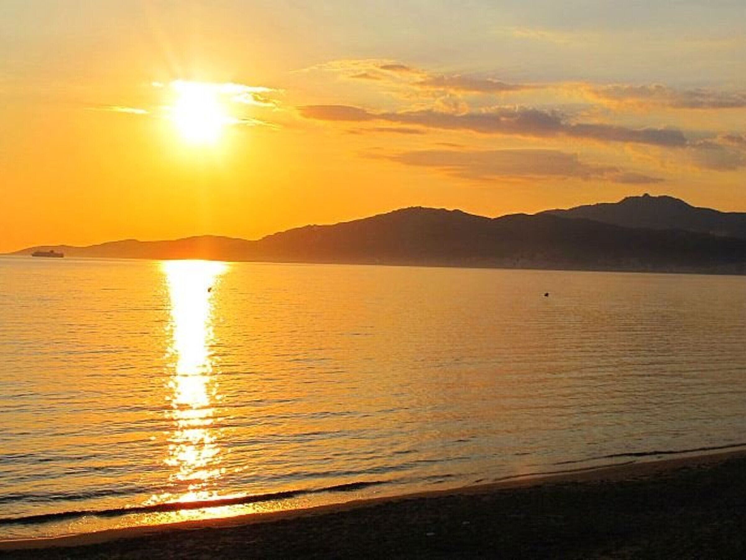 A sunset over a calm sea with distant mountains.