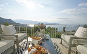A terrace with a view of the sea, outdoor seating, and a tray of pastries.
