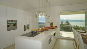 A modern kitchen with a central island, a large window with a view of the sea, and a dining area with a table and chairs. - Villa Dolce Bellezza (Salò)