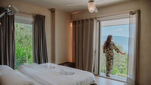A hotel room with a large bed, a small table, and a view of greenery through the window. - Villa Dolce Bellezza (Salò)