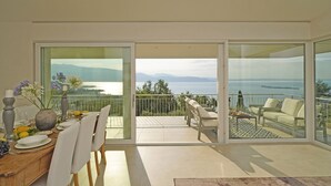 A modern dining area with a view of the sea and mountains through large glass doors. - Villa Dolce Bellezza (Salò)