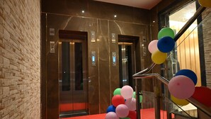 An elevator with a red carpet leading to it, and a wall with a textured pattern. - The Triumph Hotel (Varanasi)