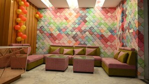 A modern lounge with a colorful geometric wall, a sectional sofa, and a glass coffee table. - The Triumph Hotel (Varanasi)