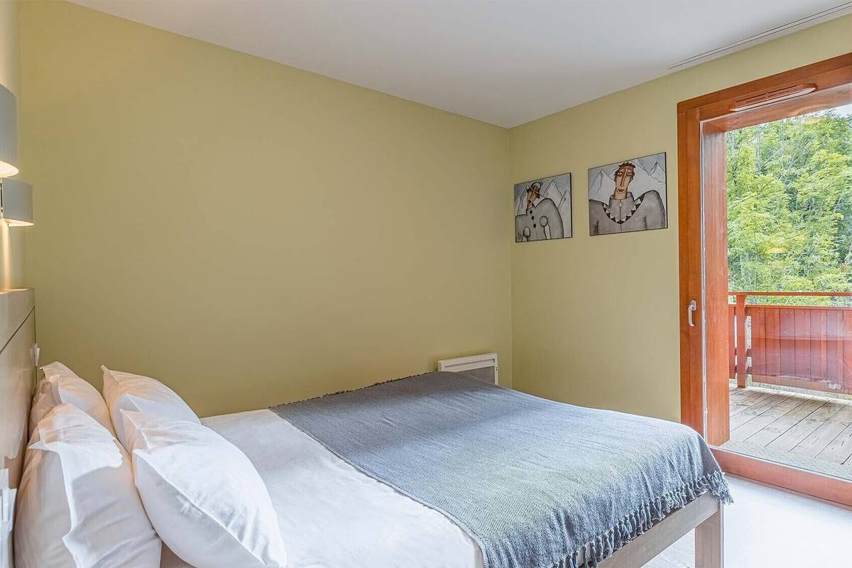 Ein Schlafzimmer mit Bett, Kissen, einem Nachttisch und einer Tür, die auf einen Balkon führt.