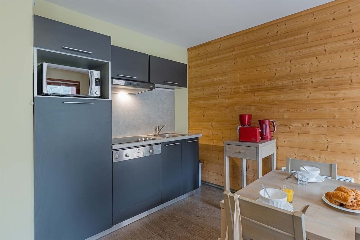 Eine moderne Küche mit grauen Schränken, einer eingebauten Mikrowelle und einer Holzwand.