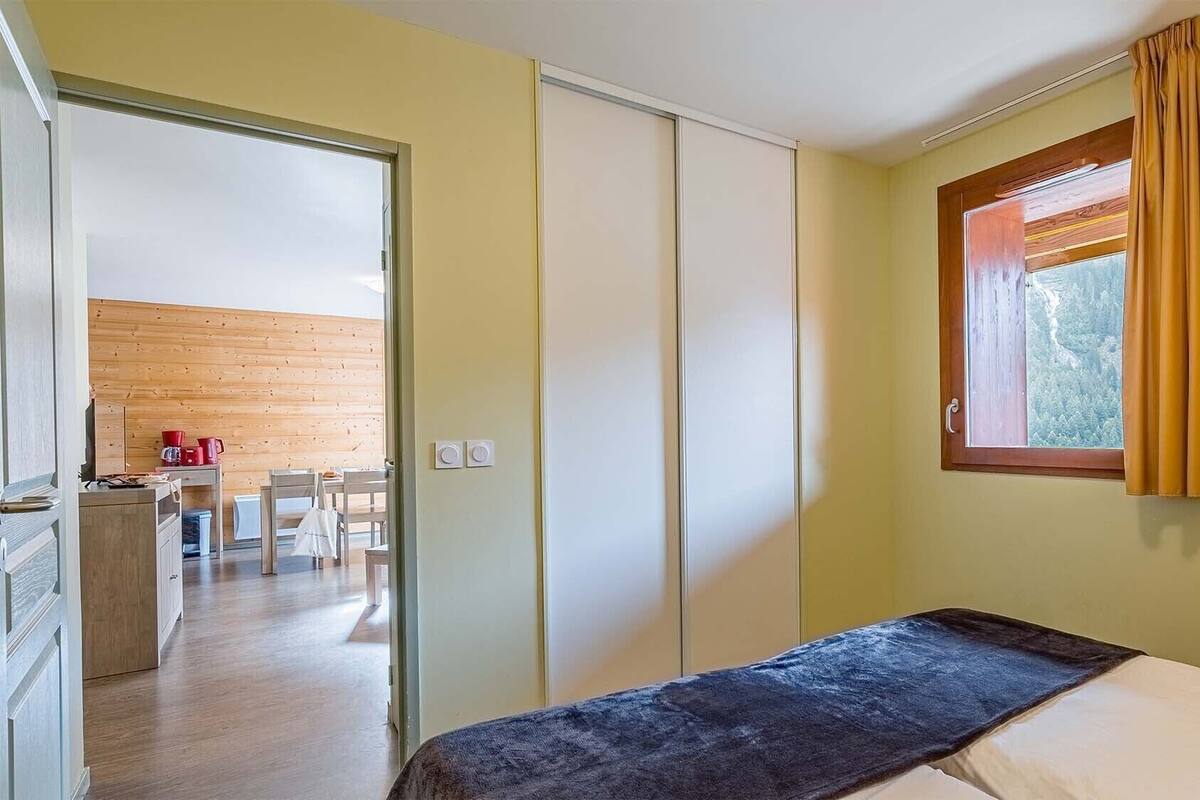 Ein Schlafzimmer mit Bett, einem fensterförmigen Ausblick und Holzwänden, mit Blick auf einen Essbereich.