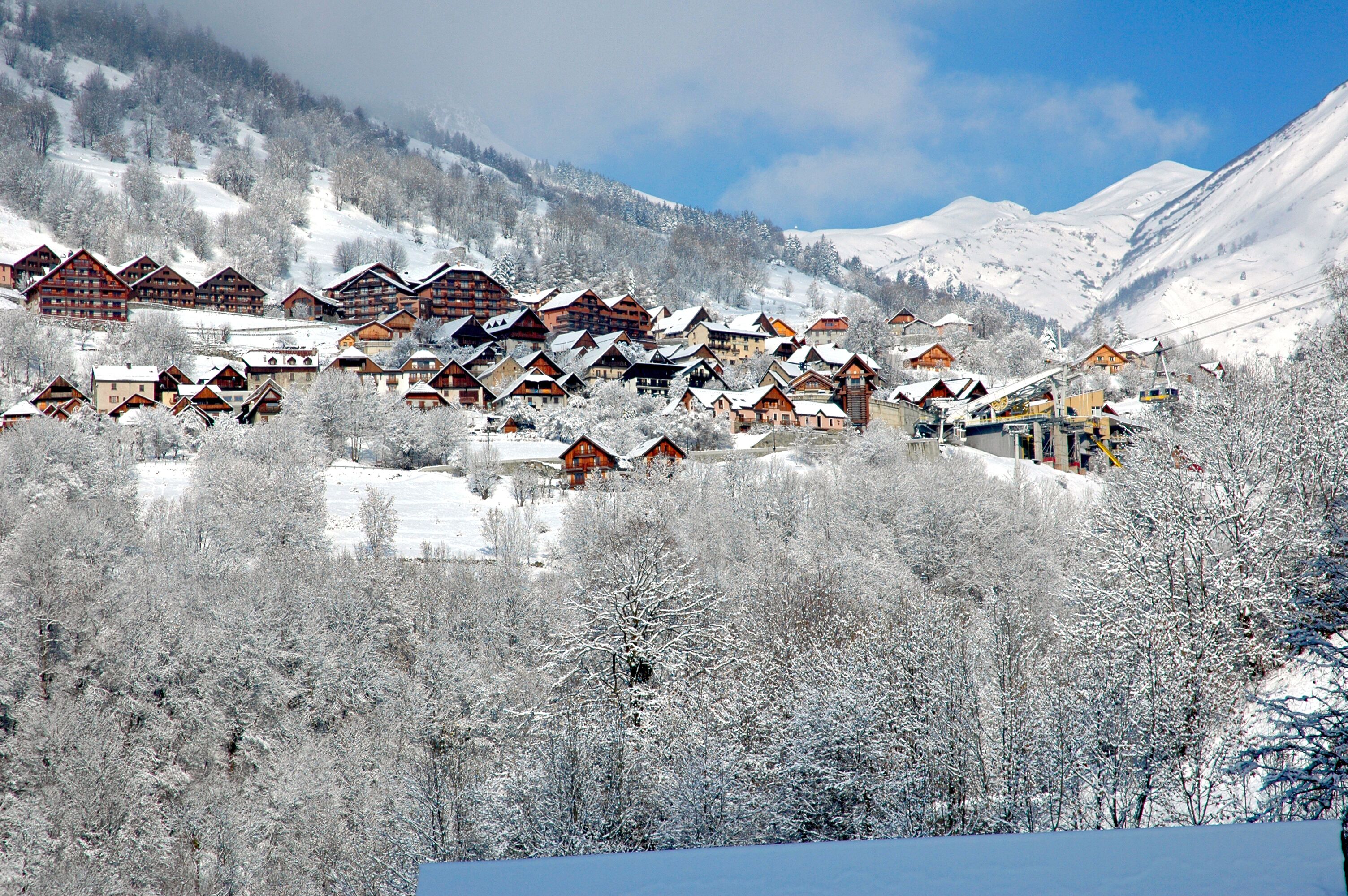 Un pueblo cubierto de nieve con edificios de madera, un telesilla y montañas al fondo.