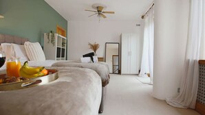 A bedroom with two beds, a ceiling fan, a wardrobe, and a bedside table with a tray of fruit and juice.