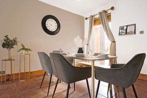 A dining area with a table set for four, a clock on the wall, and a window with curtains.