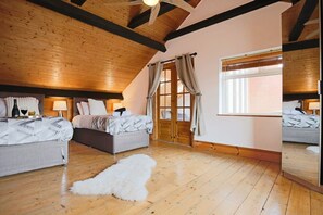 A bedroom with two beds, wooden beams, a large window, and a mirror.