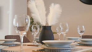 A dining table set with plates, glasses, and a vase with white feathers.