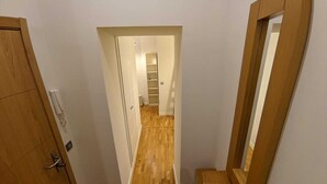 A narrow hallway with wooden flooring, a wooden door on the left, and a mirror on the right.