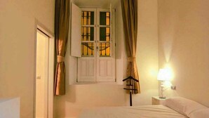A bedroom with a large bed, a chandelier, a window with curtains, and a bedside lamp.