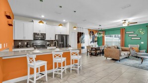 Una cucina moderna con mobili bianchi, un'isola centrale con sgabelli da bar e un'area pranzo con una parete verde.