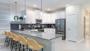 A modern kitchen with white cabinets, a large island with bar stools, stainless steel appliances, and pendant lighting. - Elegant Estate for Large Groups 5782 (Davenport)
