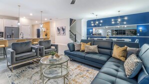 A modern living room with a blue sofa, grey armchairs, and a glass coffee table. - Elegant Estate for Large Groups 5782 (Davenport)