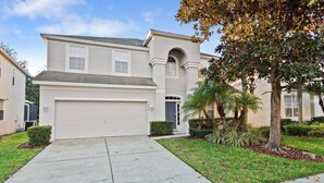 A two-story house with a garage, a front entrance, and a small front yard with a palm tree. - Luxury Private Villa With Pool on Windsor Hills Resort, Orlando Villa 5785 (Kissimmee)