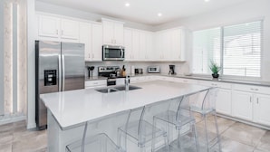 A modern kitchen with white cabinets, stainless steel appliances, and a large island with bar stools. - Rent the Perfect 4 Bedroom Townhome on Solara Resort, Orlando Townhome 5781 (Kissimmee)