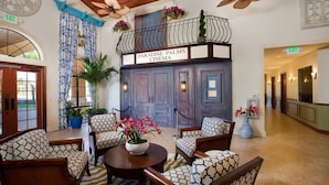 Un hall d’entrée avec un espace salon, un balcon orné d’une enseigne indiquant « Paradise Palms Cinema », et un couloir avec des portes et des luminaires.