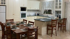 A modern kitchen with white cabinets, a dining table set with chairs, and a wooden ceiling.