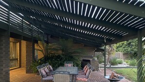 An outdoor patio with a brick floor, a table with chairs, and a built-in fireplace.