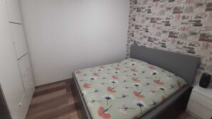 Une petite chambre à coucher avec un lit simple, une armoire et un mur recouvert d’un papier peint à motifs.