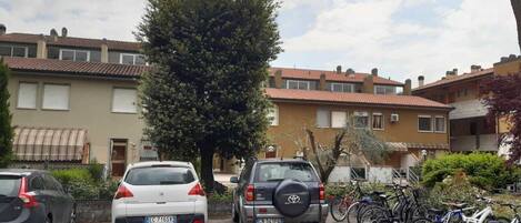 A parking area with cars and bicycles, surrounded by residential buildings with tiled roofs.