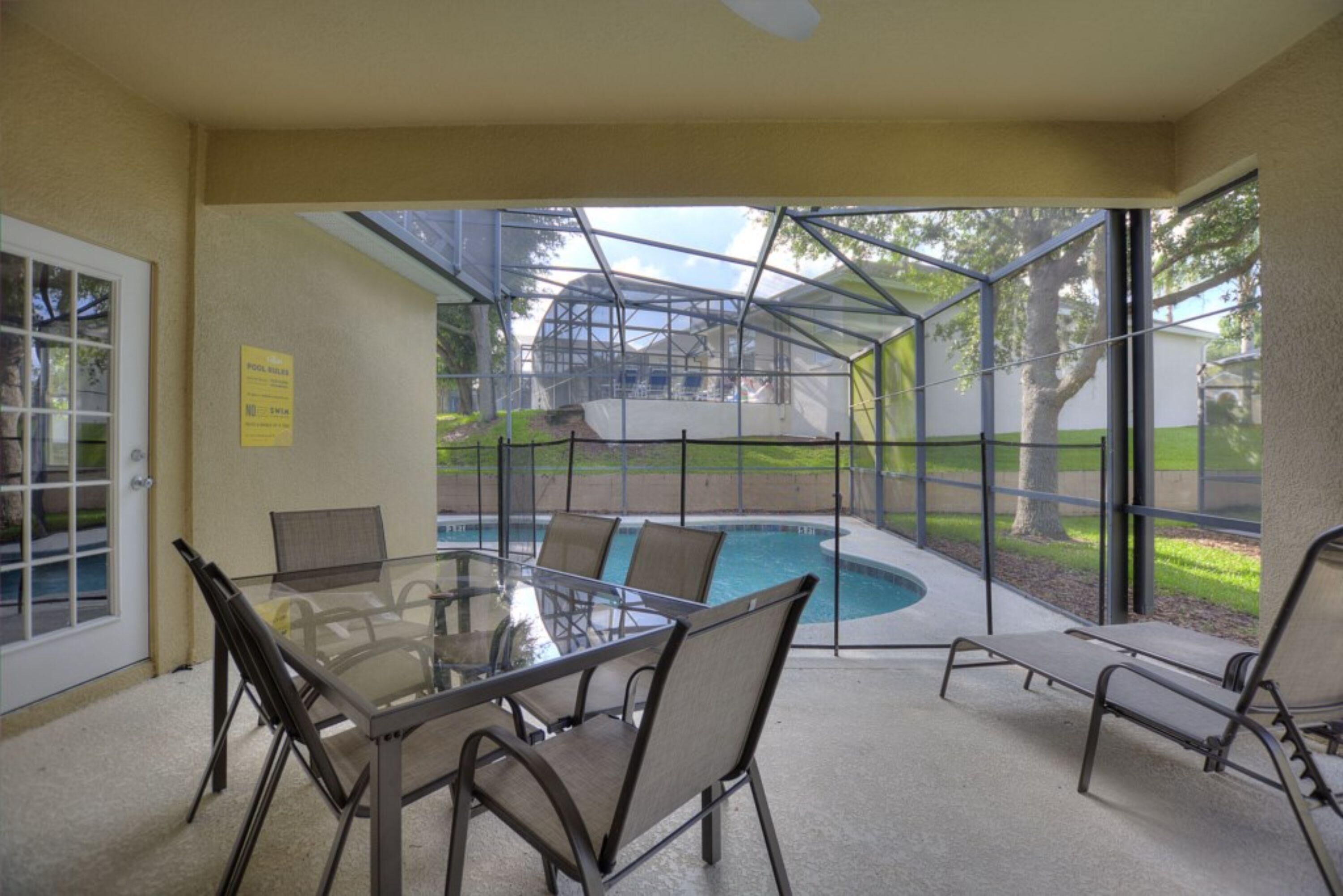 A glass-enclosed patio with a pool, a table with chairs, and a sign on the wall.