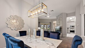 A dining room with a marble table, blue upholstered chairs, and a modern chandelier.