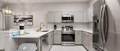 A modern kitchen with white cabinetry, stainless steel appliances, and a marble floor.
