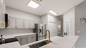 A modern kitchen with white cabinetry, stainless steel appliances, and a marble countertop.