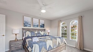 A bedroom with a wooden bed, a nightstand with a lamp, a ceiling fan, and a window with curtains.