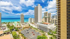 A high-rise hotel with a parking lot, a view of the ocean, and other buildings in the background. - Waikiki condo w/ balcony, pool, & beach steps away (Honolulu)