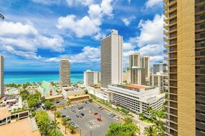 A high-rise hotel with a parking lot, a view of the ocean, and other buildings in the background.