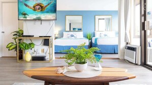 A modern hotel room with a large TV, two beds, a dining table, and a potted plant. - Waikiki condo w/ balcony, pool, & beach steps away (Honolulu)
