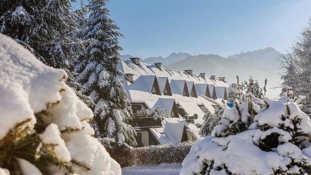 A snow-covered landscape with a row of chalet-style buildings, each with a sloped roof and multiple windows.